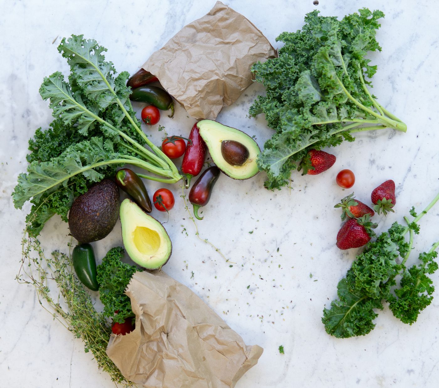 Fresh kale, avocado, tomatoes and strawberries arranged on a marble surface